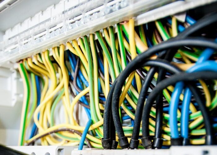 Hand of electrician working on a circuit breaker panel with colorful wires, ensuring safe electrical connections.
